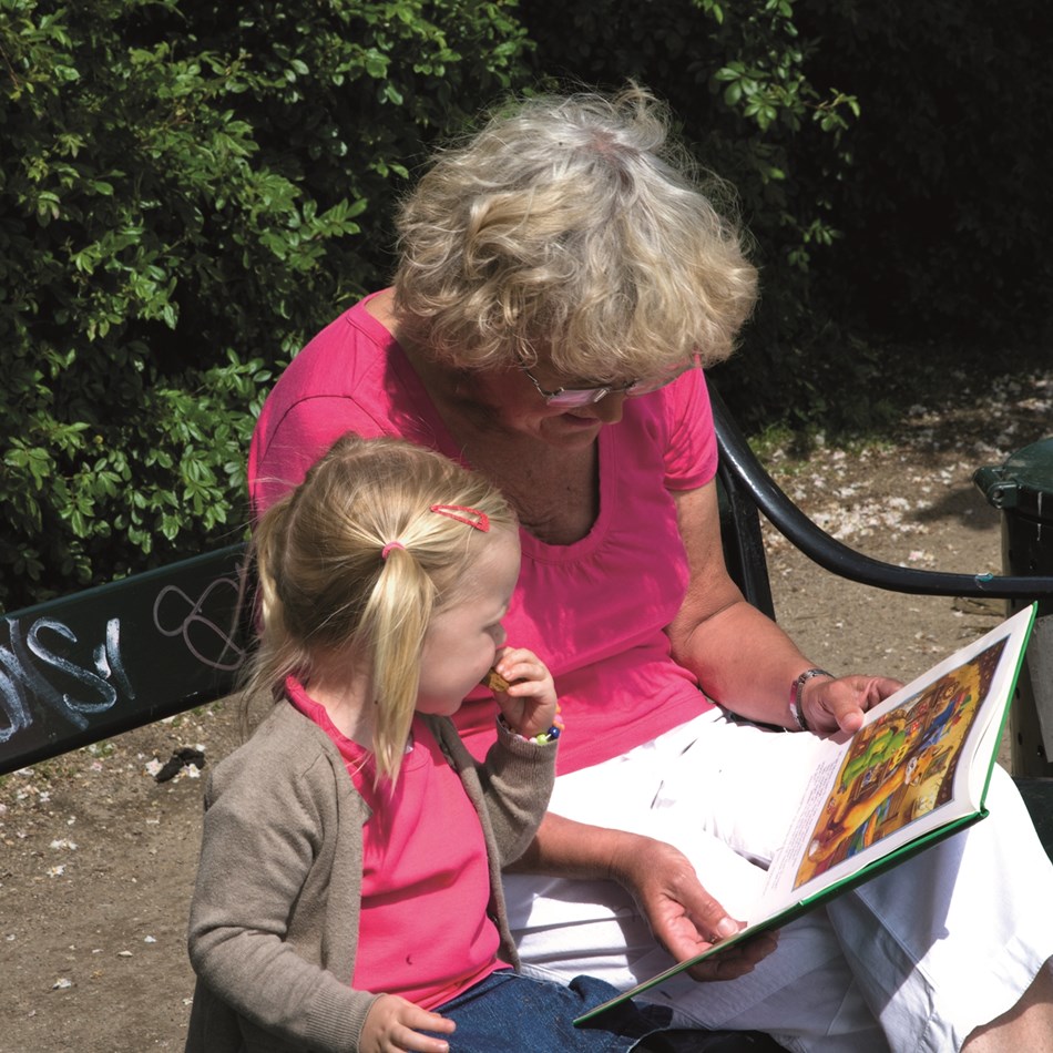 En lille pige og bedstemor læser en bog på en bænk
