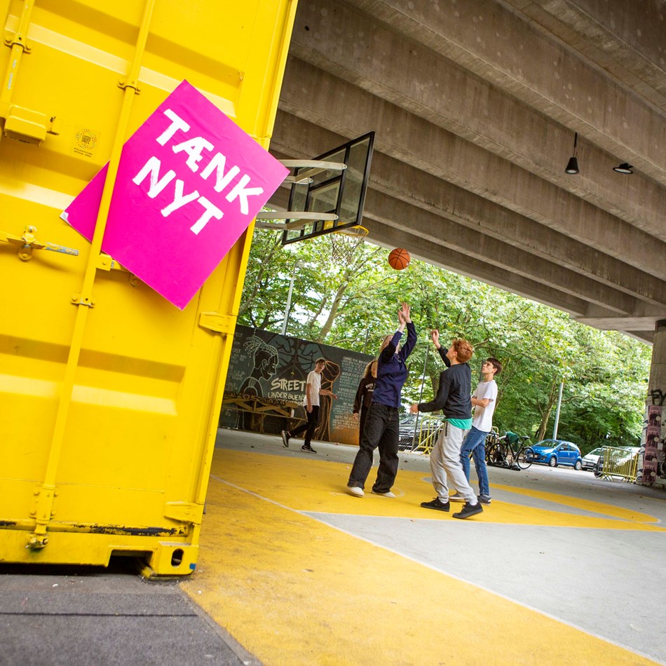 Tænk nyt-skilt ved en gul container, hvor unge mennesker spiller basket